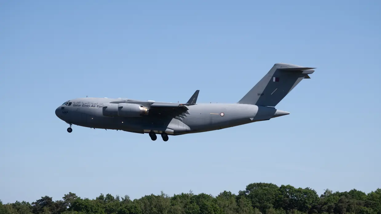 Een C-17a in de lucht met een rij bomen op de achtergrond