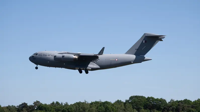 Een C-17a in de lucht met een rij bomen op de achtergrond