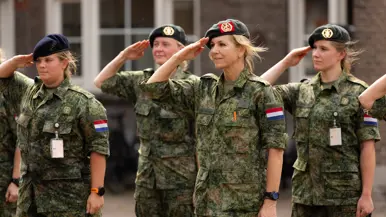 Koningin Máxima brengt met haar baret op de militaire groet tussen drie andere militairen. 