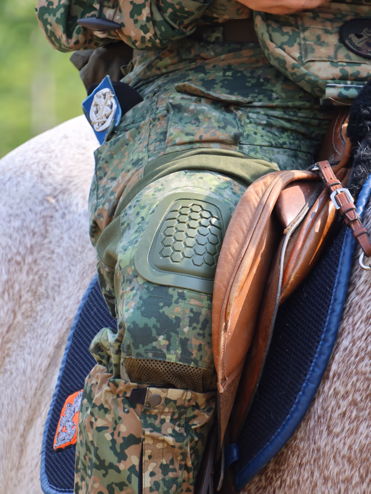 Een soldaat in camouflagekleding met een helm en kniebeschermer zit op een paard met een bruin zadel en teugels.