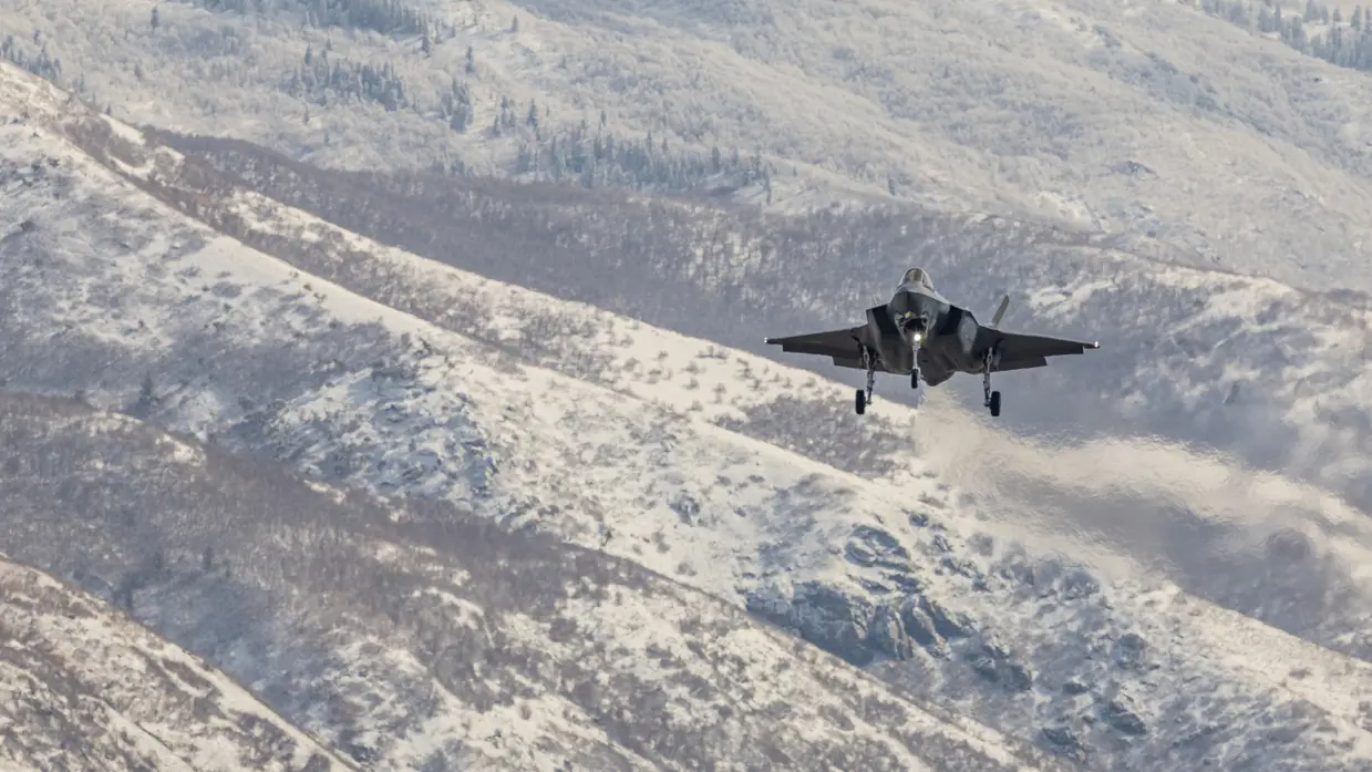 Een F-35 vliegend boven besneeuwd berglandschap.