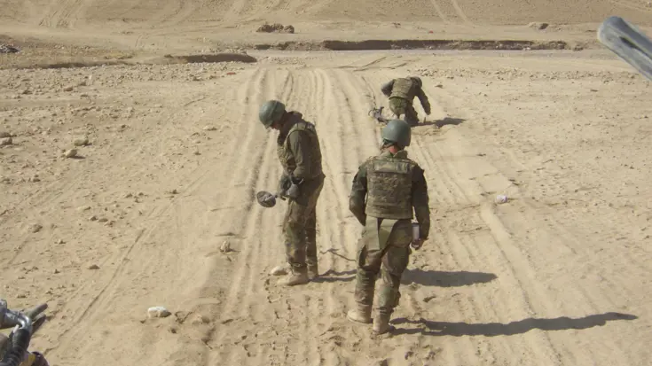 3 militairen zoeken in het Afghaanse zand naar explosieven.
