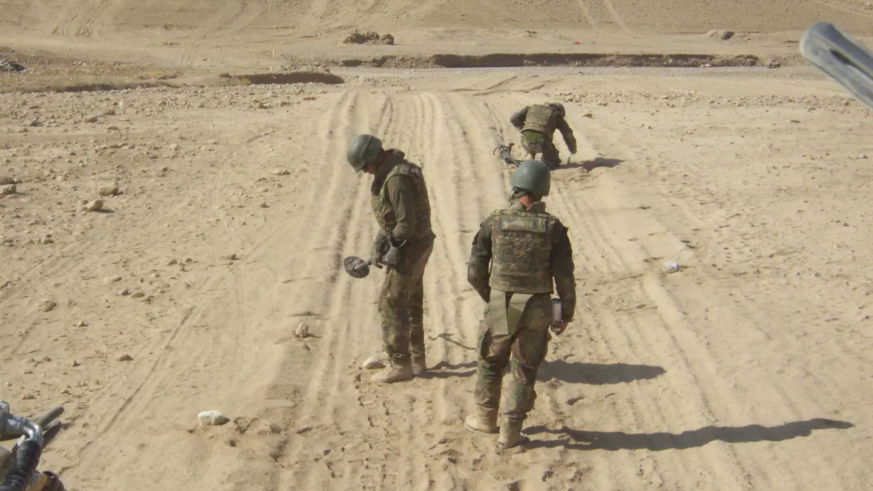 3 militairen zoeken in het Afghaanse zand naar explosieven.