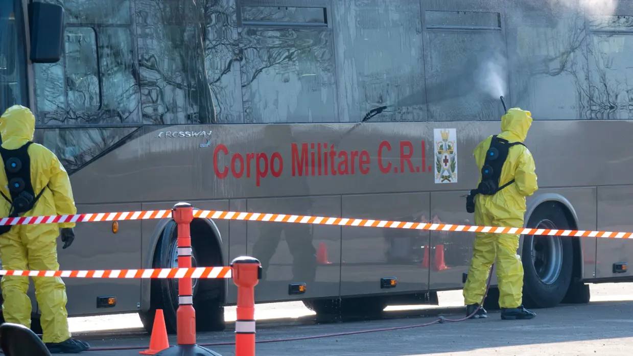 2 militairen in beschermende kleding spuiten een Italiaanse bus.