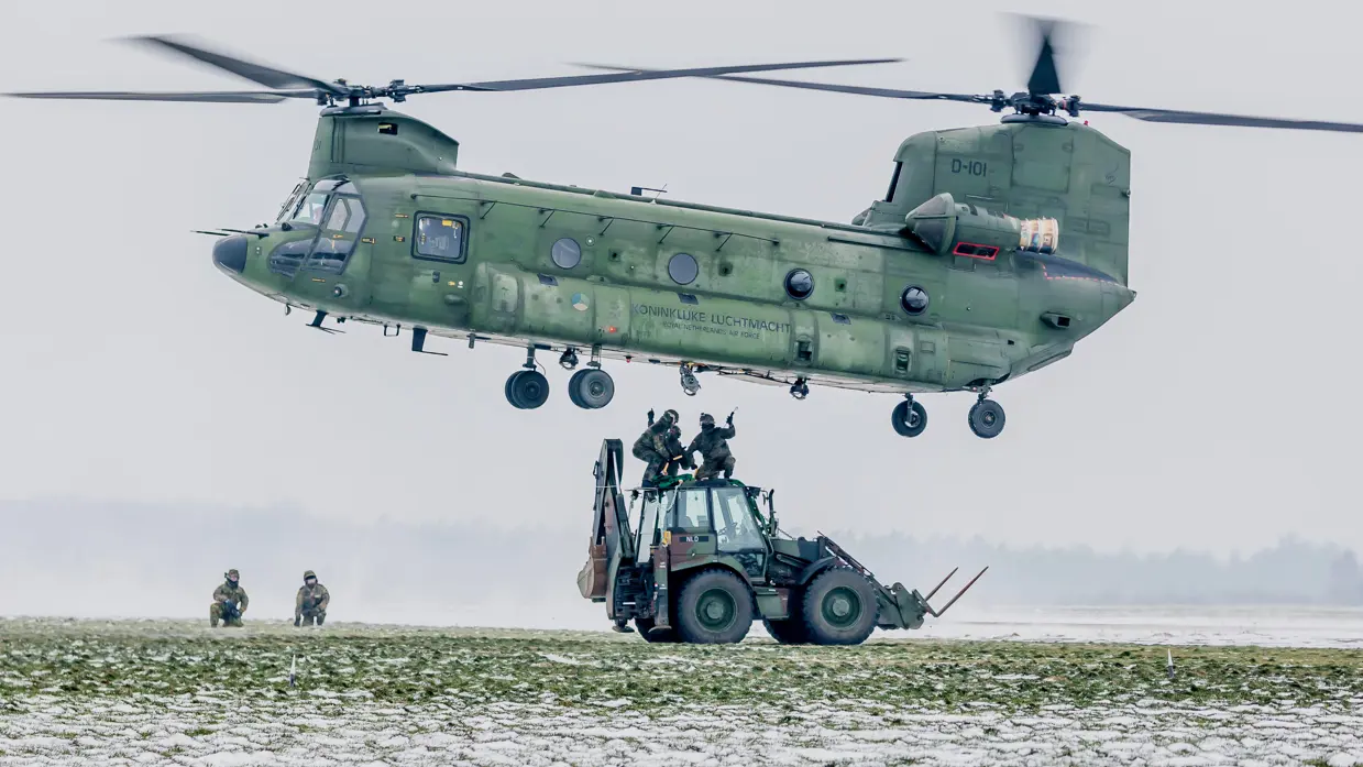 Een graaflaadcombi wordt door een Chinook-helikopter opgetild.