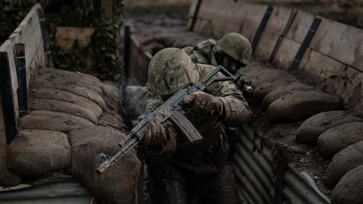 2 militairen lopen gebukt door loopgraven. De voorste militair houdt wapen voor zijn hoofd.