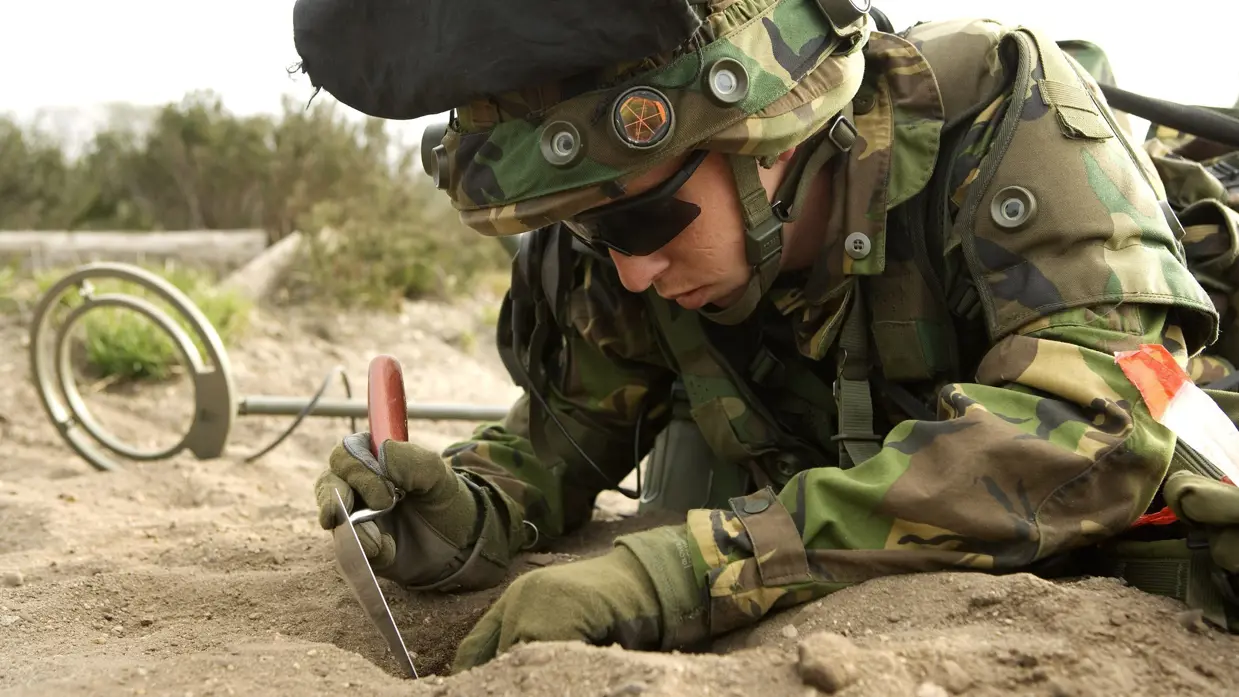 Een militair in opleiding graaft een gat in het zand.