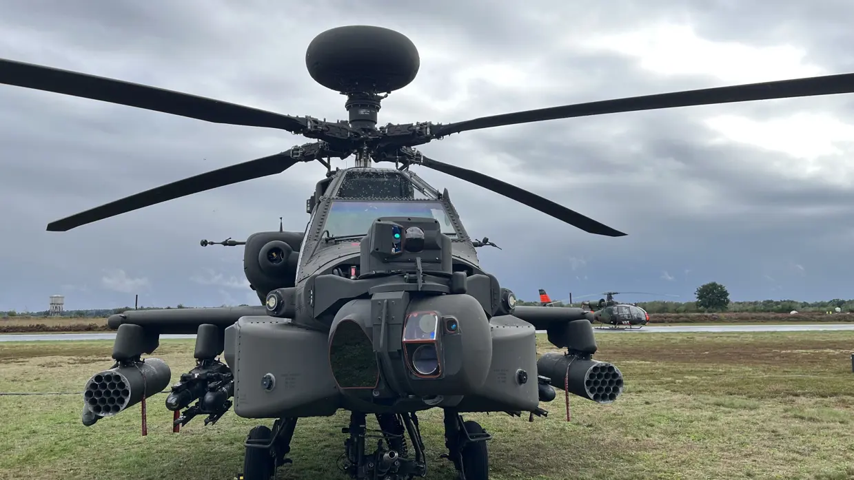 Een grote zwarte militaire helikopter staat op een betonnen baan met een grijze lucht er boven. 
