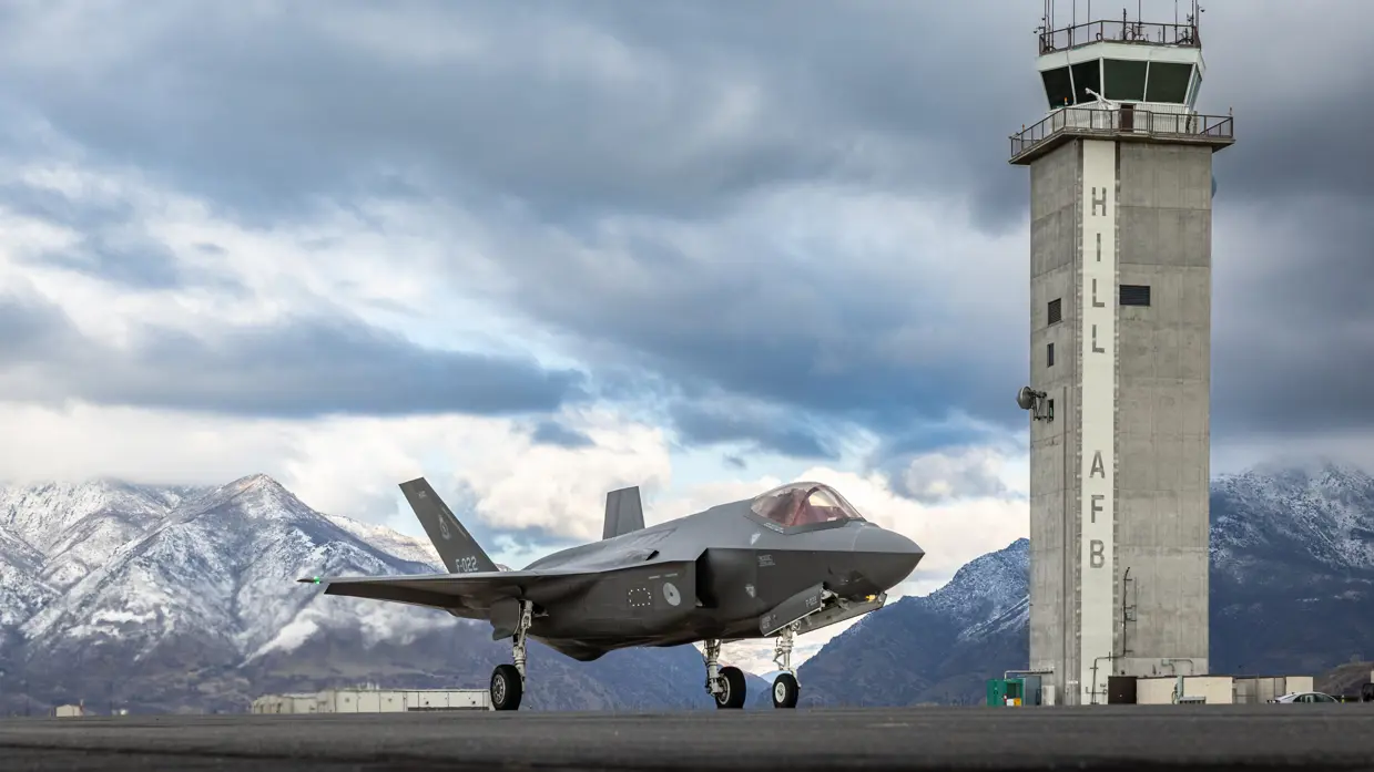 Een F-35 links van de luchtverkeerstoren waarop ‘Hill AFB’ staat. Op de achtergrond besneeuwde bergen.