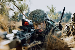 Een militair in de bosjes kijkt door een wapen.