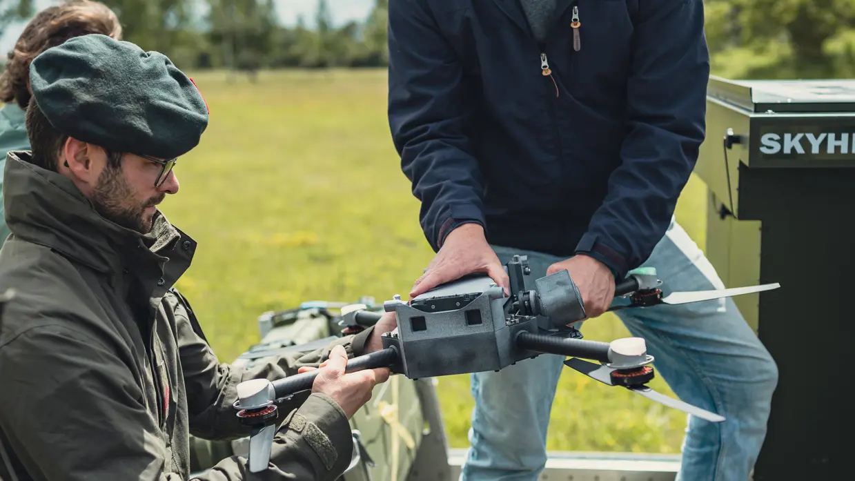 Een technuet overhandigt een drone aan een militair.