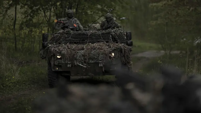 Een Fennek-verkenningsvoertuig met twee militairen rijdt door een beboste omgeving.