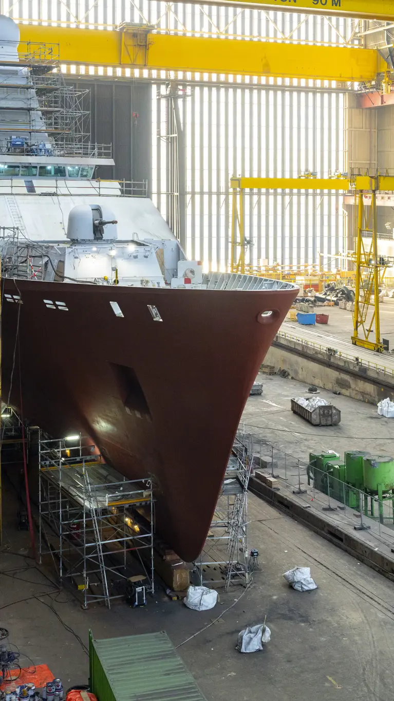 Zr.Ms. Holland in aanbouw in een overdekte scheepswerf, omringd door steigers, kranen en bouwmateriaal. 