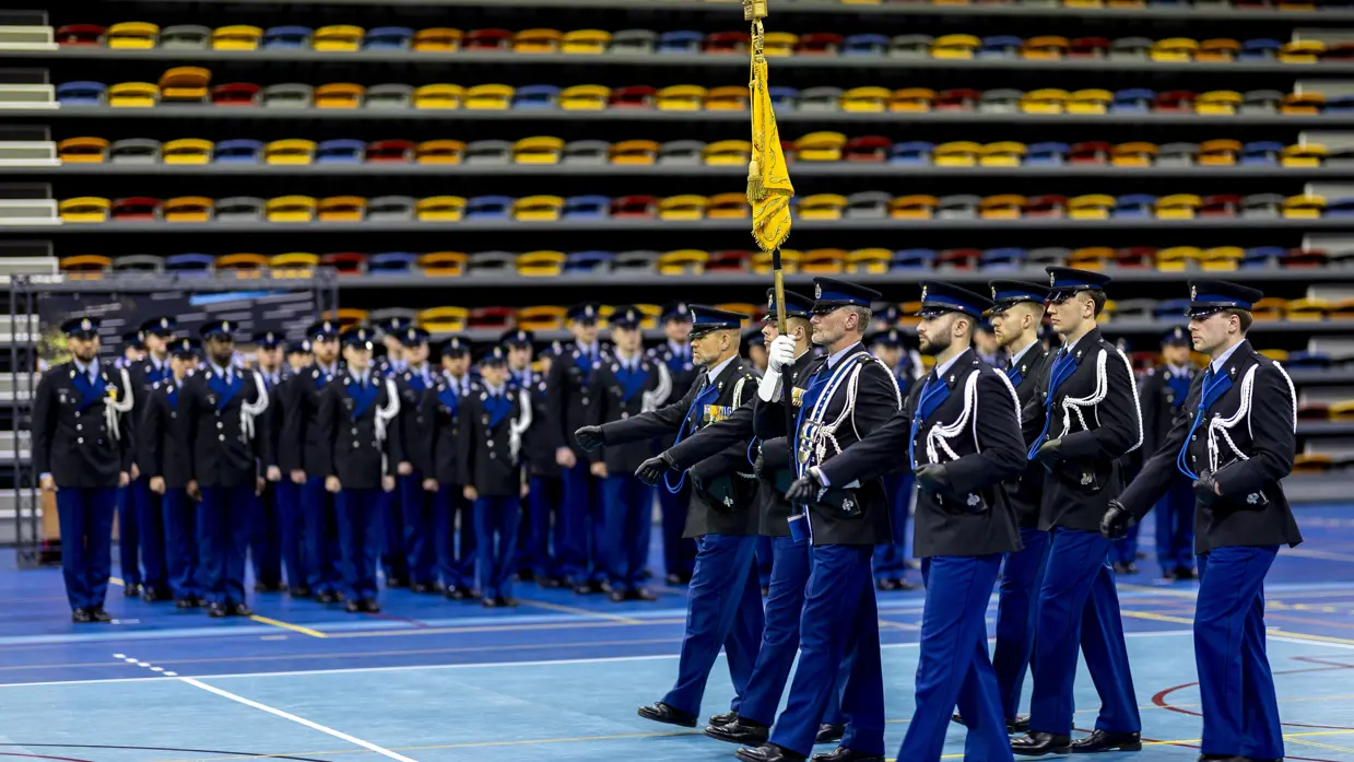 Marechaussees in ceremonieel tenue treden aan tijdens de beëdiging in een sporthal in Apeldoorn.