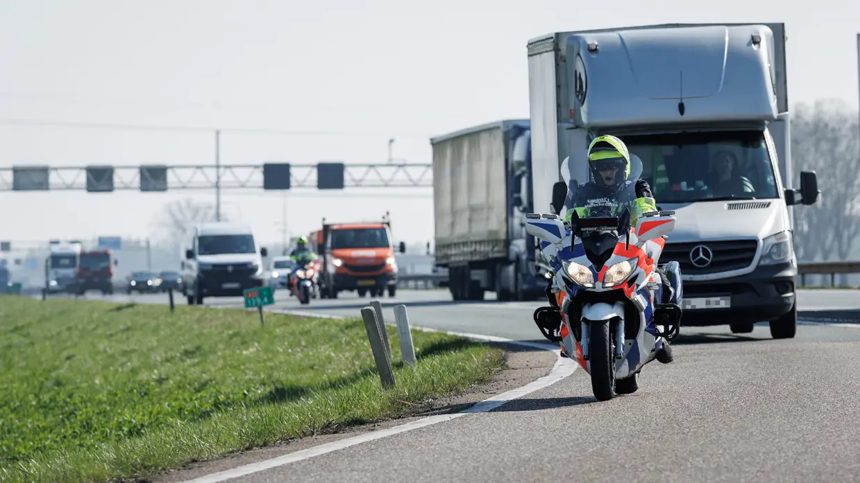 Een motor van de Koninklijke Marechaussee met daarachter een rits voertuigen.