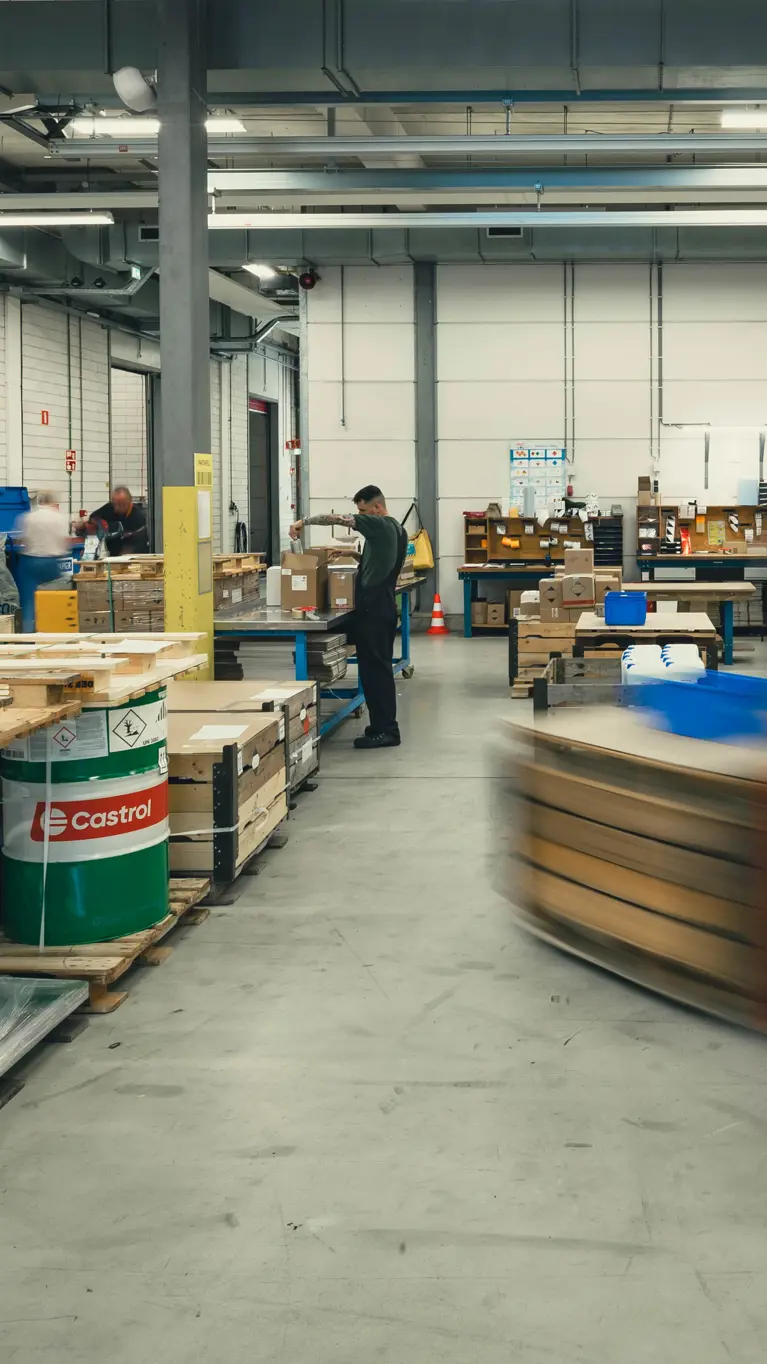 Het grijze depot van het DBBB. Hierop zijn onder meer medewerkers, pallets, vaten olie en een langsrijdende heftruck te zien.&nbsp;