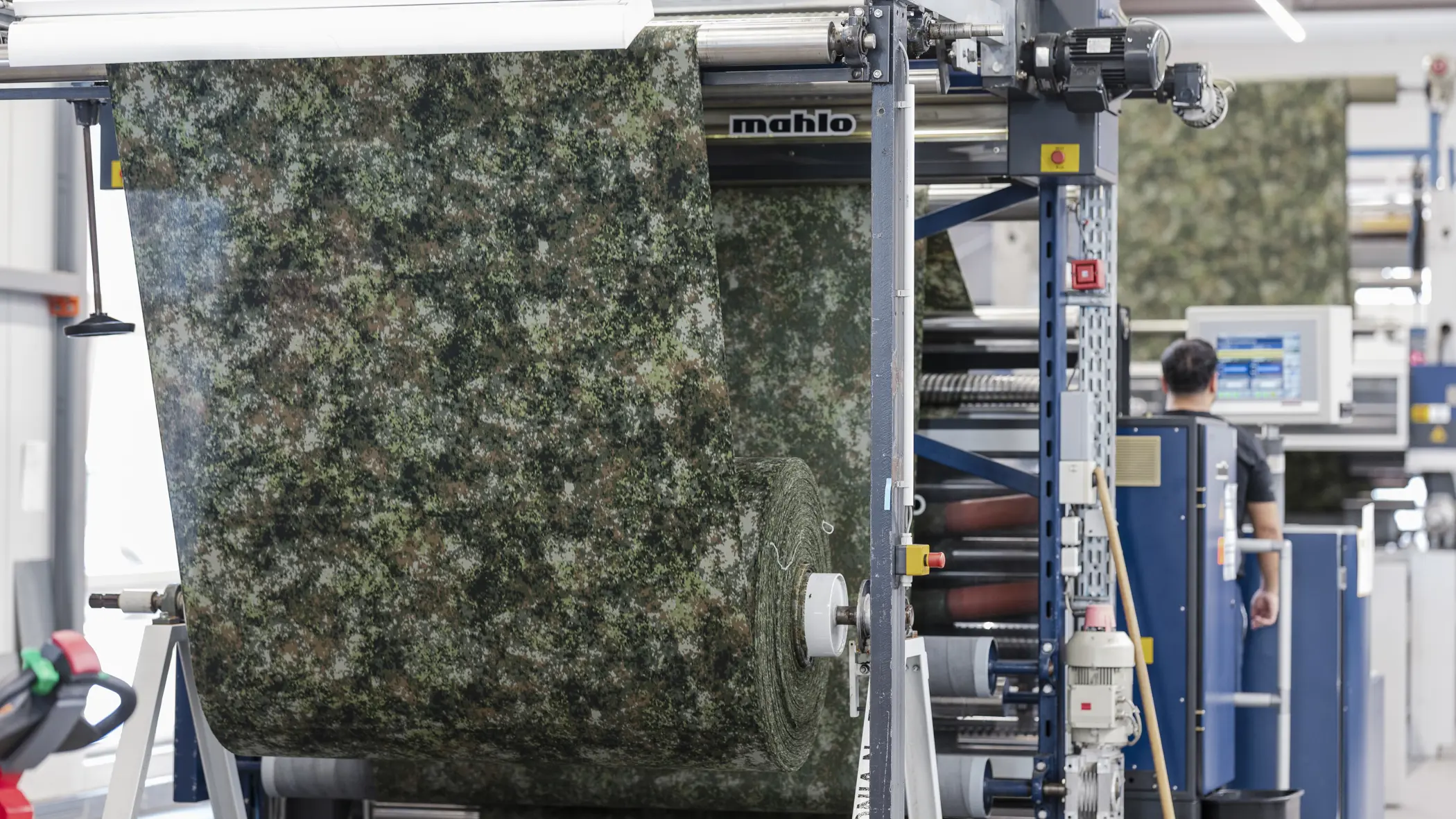 Stof met groen camouflagepatroon wordt door machine geleid tijdens een controle op productiefouten.