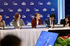 De minister zit achter een tafel met haar internationale collega's.