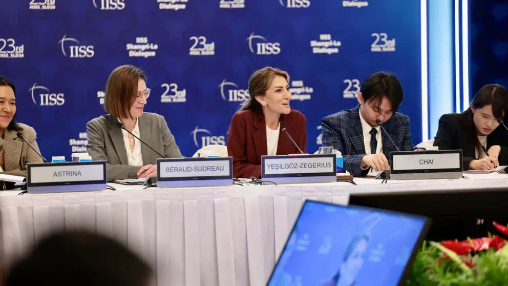 De minister zit achter een tafel met haar internationale collega's.