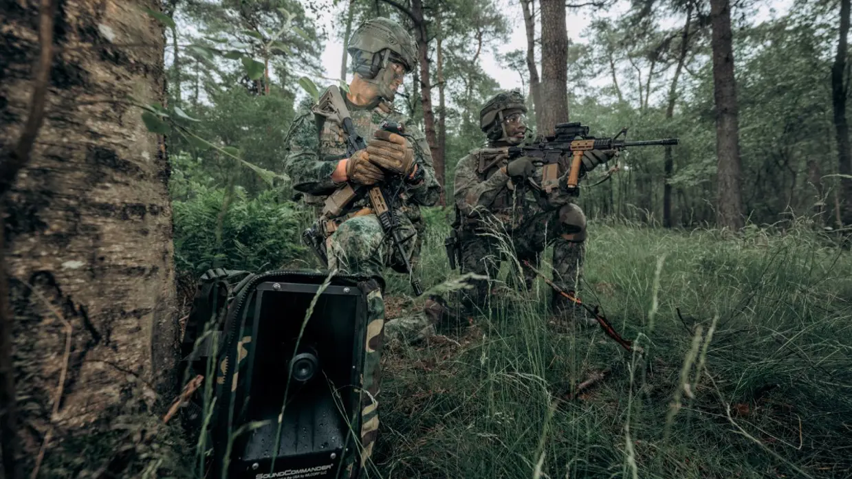 2 gecamoufleerde militairen hurkend in een bos ieder met een Colt-geweer.
