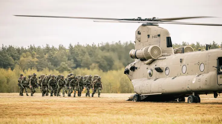 Bepakte infanteristen lopen in een veld naar een Chinook