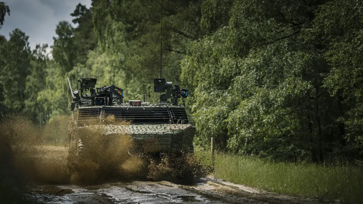 Een militair voertuig raast in het bos over een zandweg. 