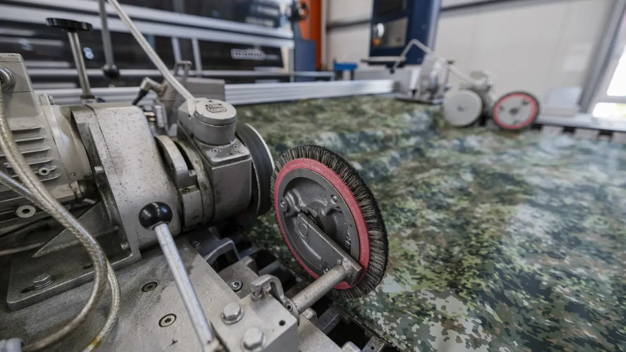 Stof met groen camouflagepatroon wordt door machine geleid tijdens controle op productiefouten.