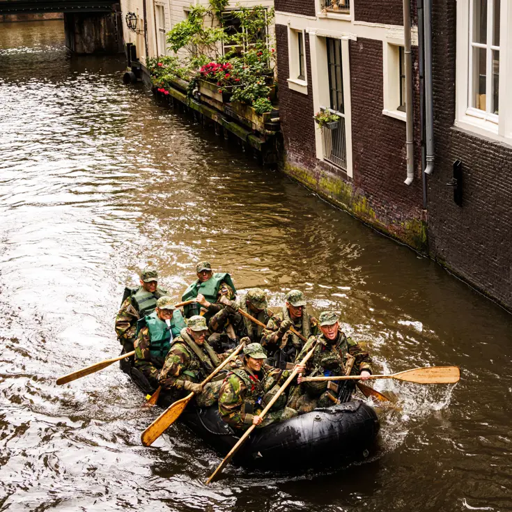 De deelnemers aan de NWT roeien in rubberboten door Amsterdam.