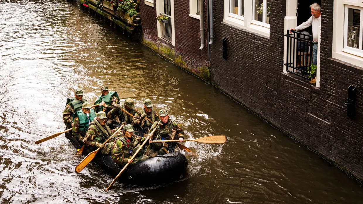De deelnemers aan de NWT roeien in rubberboten door Amsterdam.