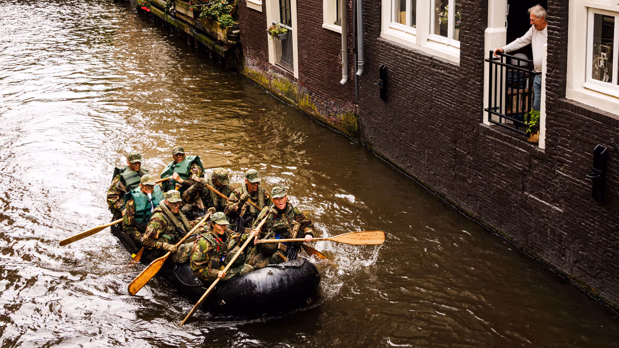 De deelnemers aan de NWT roeien in rubberboten door Amsterdam.