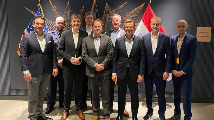 Groep mannen poseert in pak voor Nederlandse en Amerikaanse vlag.