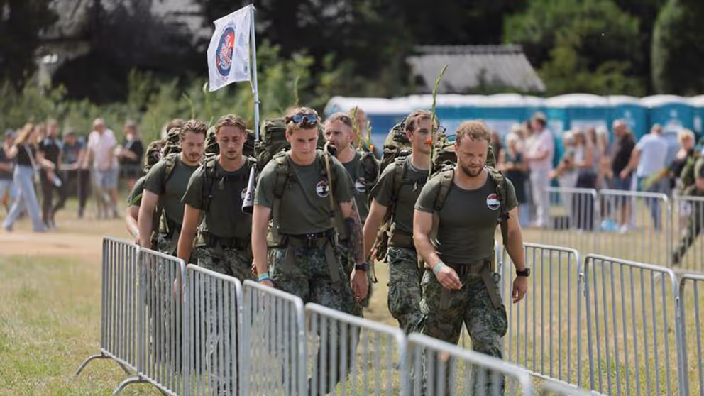 Militairen wandelen tussen dranghekken op grasveld.