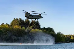 Een helikopter met bluszak hangt boven het water.