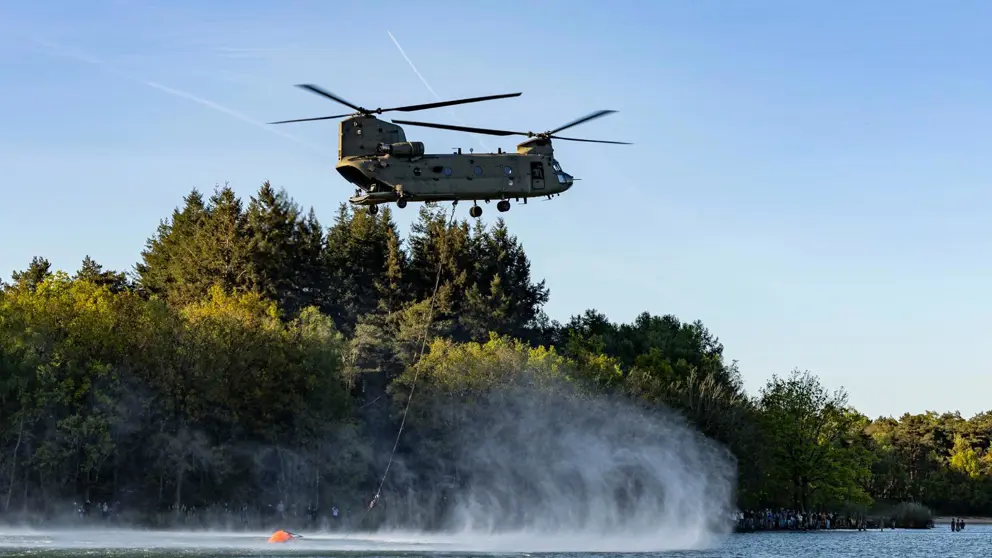 Een helikopter met bluszak hangt boven het water.
