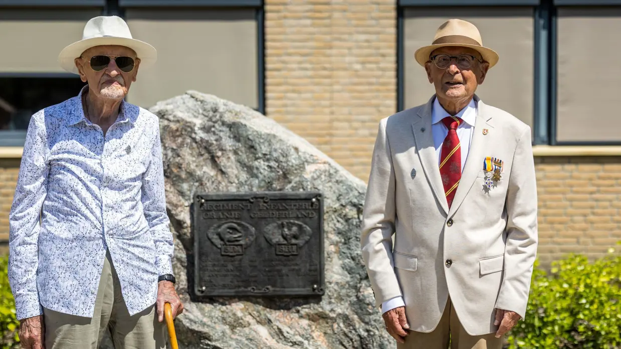 2 veteranen poseren naast een gedenksteen.&nbsp;