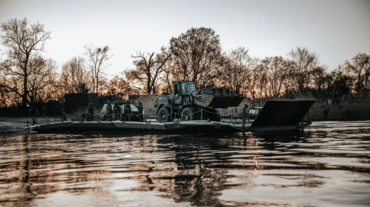 Een pontonbrug (dit is een tijdelijke brug) over het water met op de brug meerdere militairen en een voertuig.