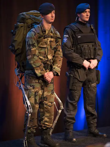 Twee mannen in uniform: één met camouflage, rugzak en exoskelet, de andere in zwart met kogelwerend vest.