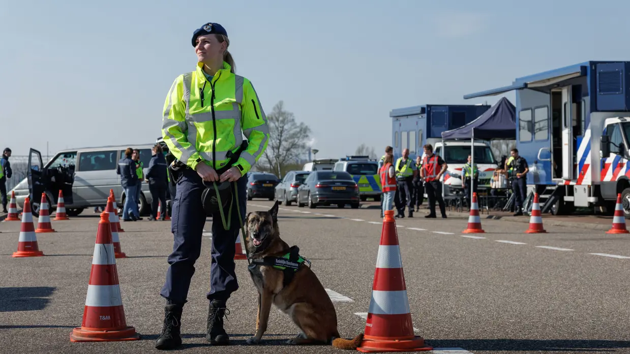 Een vrouwelijke marechaussee met een hond aan haar zijde.