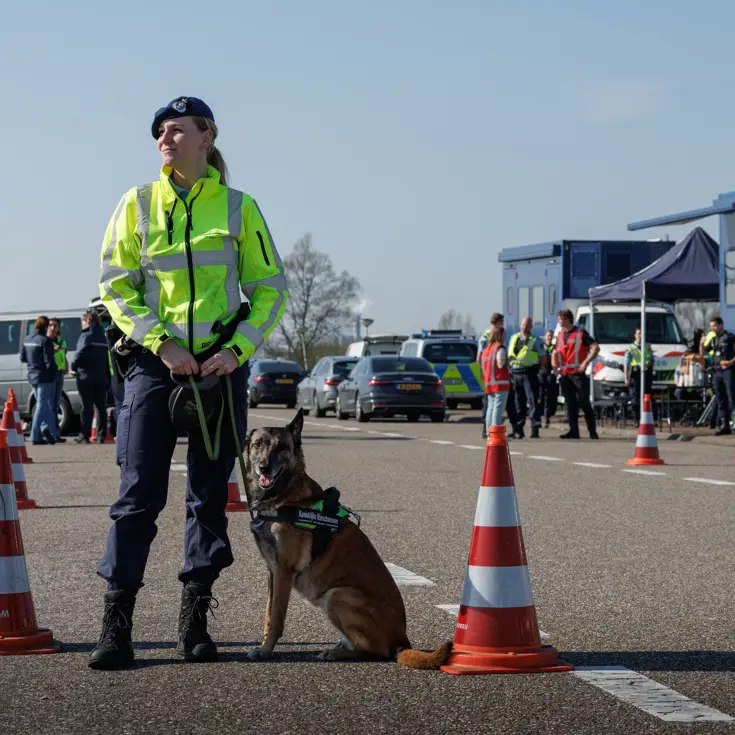Een vrouwelijke marechaussee met een hond aan haar zijde.