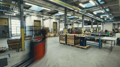 Een grijze loods met daarin diverse lange tafels en een langsrijdende heftruck.