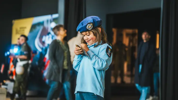 Klein meisje in Marechaussee-uniform met een boekje in haar hand.