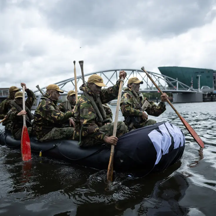De deelnemers aan de NWT roeien in rubberboten door Amsterdam.