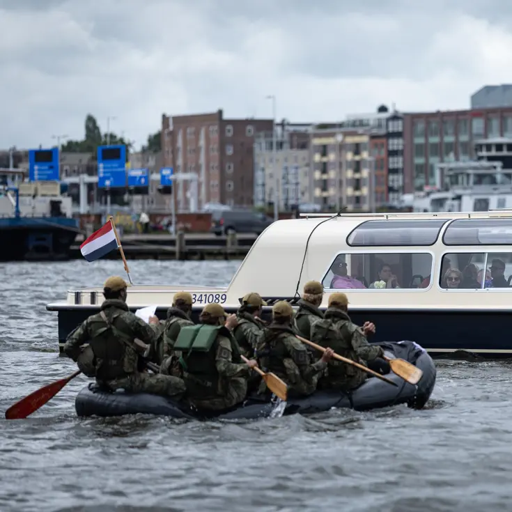De deelnemers aan de NWT roeien in rubberboten door Amsterdam.