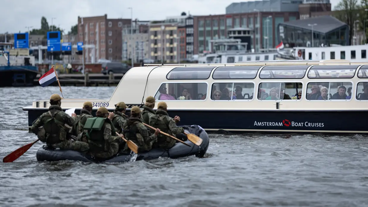 De deelnemers aan de NWT roeien in rubberboten door Amsterdam.