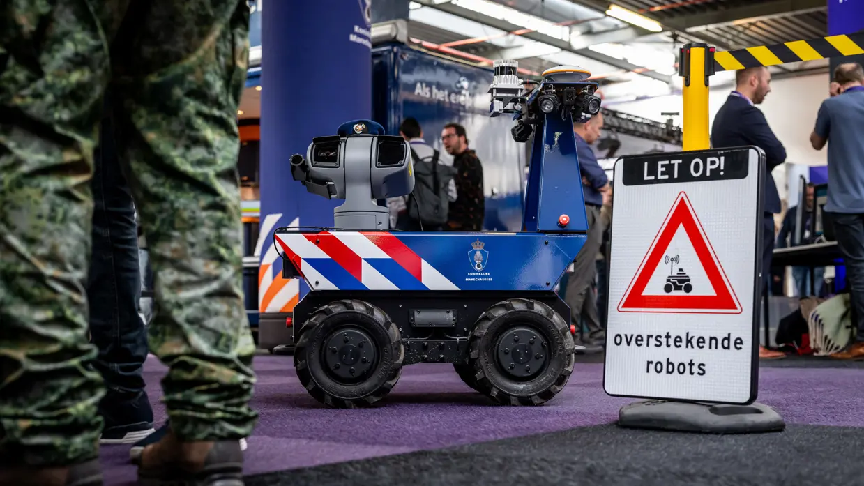 Een onbemand voertuig rijdt over een beursvloer met op de voorgrond een waarschuwingsbord.