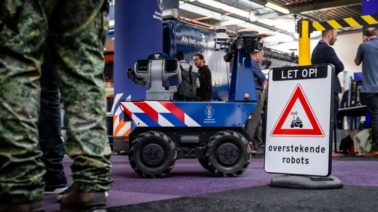 Een onbemand voertuig rijdt over een beursvloer met op de voorgrond een waarschuwingsbord.
