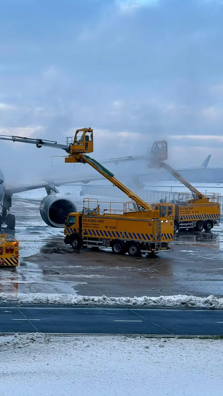Een vliegtuig op een besneeuwde luchthaven, waar gele de-icing voertuigen met lange armen ijs van de vleugels verwijderen voor een veilige vlucht.