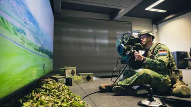Een viertal afbeeldingen. Naast het cilindervormige, donkergroene antitankwapen Spike Long Range gericht op een beamer, hetzelfde middel alleen nu met daarachter een militair. Samen met een instructeur, die achter een beeldscherm zit, bevinden de twee zich in een kleinere ruimte. Vervolgens diezelfde oefenende militair schuin vanaf onder en gezien vanaf voren. Daarbij is zijn geconcentreerde blik zichtbaar.
