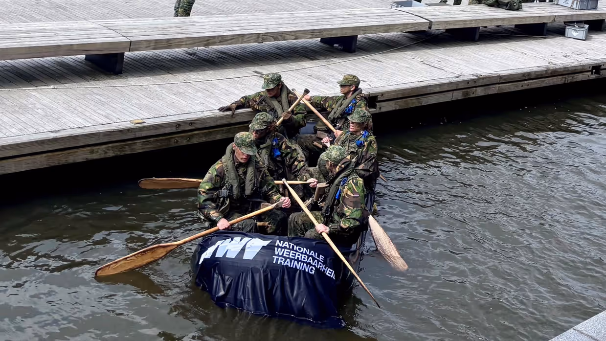 De deelnemers aan de NWT roeien in rubberboten door Amsterdam.