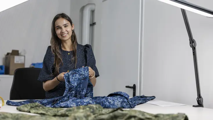 Een vrouw achter werktafel controleert militaire uniformen. In dit geval een blauw marine-uniform.